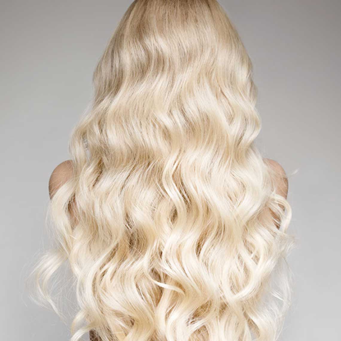 Lange, wellige, platinblonde Haare aus der Rückenansicht vor neutralem Hintergrund.